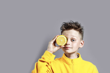 a boy in a bright yellow jacket with a lemon in his hand on a blue backgroundの写真素材