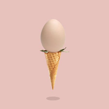 Concept on the theme of Easter 2022, egg as a symbol of the holiday in an ice cream cone on a pink background with a shadow, postcardの写真素材
