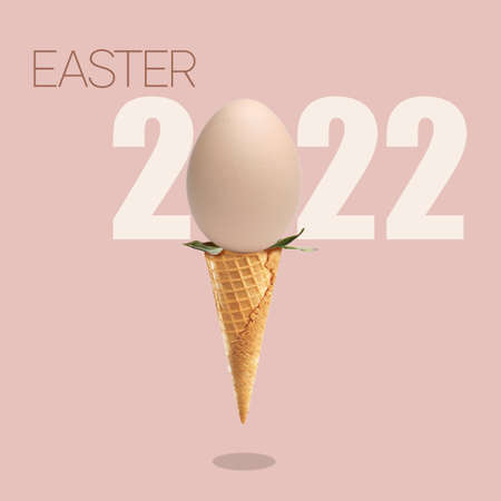 Concept on the theme of Easter 2022, egg as a symbol of the holiday in an ice cream cone on a pink background with a shadow, postcardの写真素材