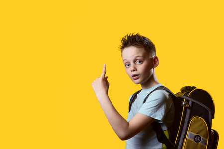 A first-grader schoolboy back to school in September with a backpack and textbooks on a yellow background, autumn concept.の写真素材