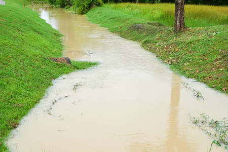 Small wooden bridge over the small lake canal through garden and golf course with green grass and concrete cart path and walk way beside.の写真素材