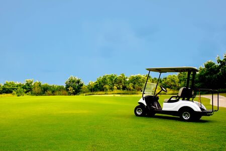 Golf cart car in fairway of golf course with fresh green grass field and cloud blue sky and treeの写真素材