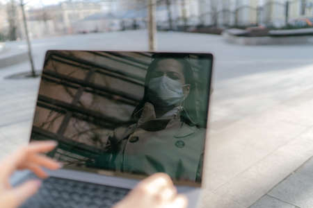 Girl sits on the street wearing a medical mask and works behind a laptop during a pandemicの写真素材