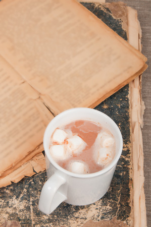 Cup of coffee with marshmallows on vintage books on linen backgroundの写真素材