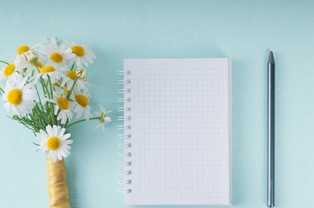 Blank notebook, a pencil and a bouquet of daisiesの写真素材