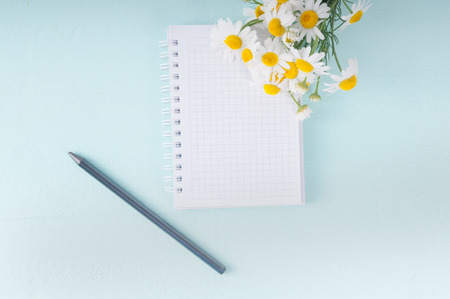 Blank notebook, a pencil and a bouquet of daisiesの写真素材