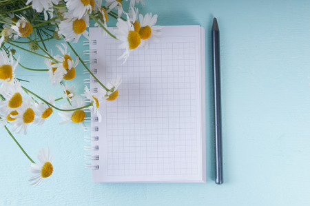Blank notebook, a pencil and a bouquet of daisies