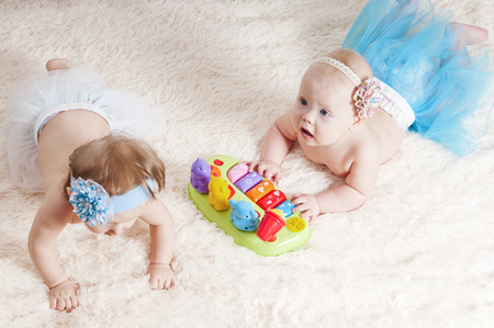 Two little girls playing in the children's room on the carpet near the bedsの写真素材