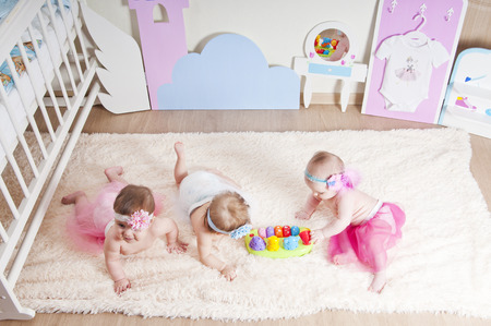 Three little girls playing in the children's room on the carpet near the bedsの写真素材