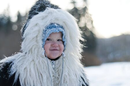 Little girl in a fur coat walks in the winter park