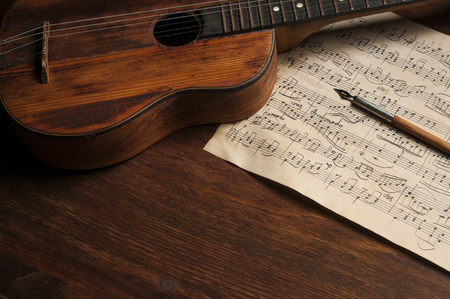 Ancient little acoustic guitar and hand-written notes on the tableの写真素材