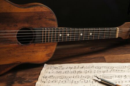 Ancient little acoustic guitar and hand-written notes on the tableの写真素材