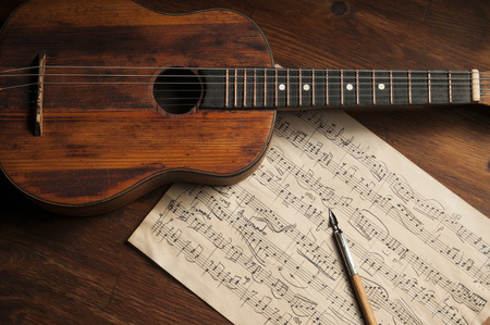 Ancient little acoustic guitar and hand-written notes on the tableの写真素材