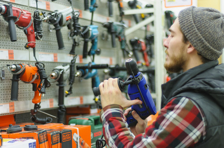EKATERINBURG, RUSSIA - JANUARY, 8, 2018: A young man chooses powerful drill in the hardware store
