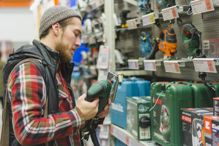 EKATERINBURG, RUSSIA - JANUARY, 8, 2018: A young man chooses electric jig saw in the hardware store