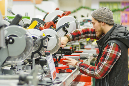 A young man chooses miter saw in the hardware storeの写真素材