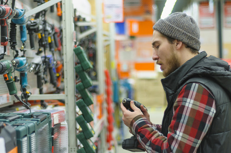 A young man chooses cordless screwdriver in the hardware storeの写真素材