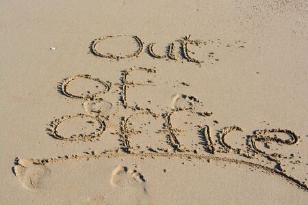 Out of office text written in sand on a beach suggesting work life balanceの写真素材