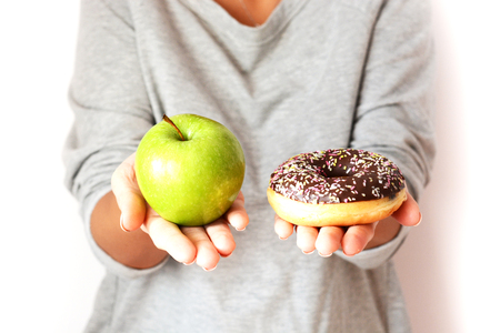Healthy lifestyle or nutrition concept with young woman holding in hands an green apple and a donutの写真素材