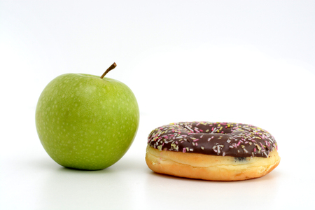 Close-up of tasty chocolate donut and fresh green apple on white background suggesting healthy eating conceptの写真素材