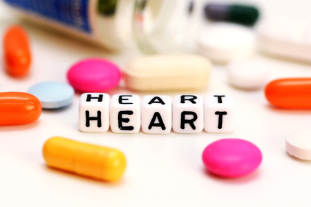 Multicolored medical drugs and letter cubes spelling heart, suggesting cardiac problemsの写真素材
