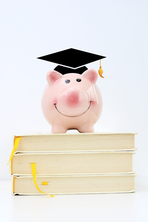 Piggy bank wearing a graduate cap standing on top of a pile of books. Saving for higher education conceptの写真素材