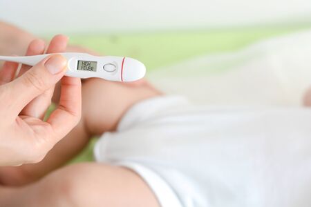 Checking baby temperature which indicates high fever on thermometerの写真素材