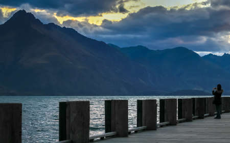 A woman taking photo on wooden pier, Queenstown, New Zealandの写真素材