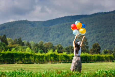 A girl playing balloon in grass field with mountain backgroundの写真素材