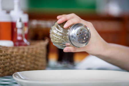 shaking oregano spices in to the dish with restaurant background