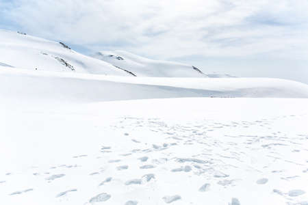 Lots of footprints in the snow covered mountain under cloudy skyの写真素材