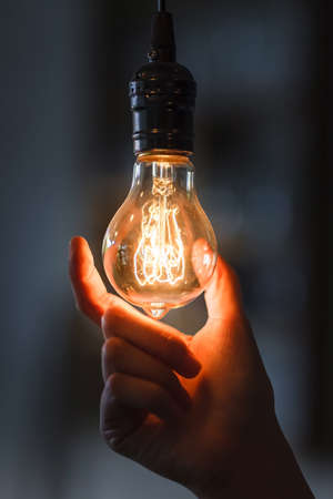 Lightbulb with filament held in woman hand on dark backgroundの写真素材