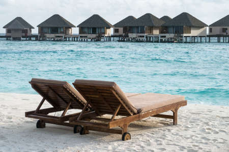 Wooden chairs at white sand beach with water villas background, Maldivesの写真素材