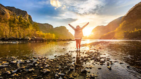 Woman facing to sunrise at river around with mountain, Norway