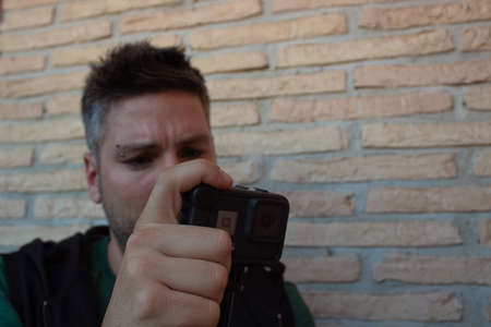 Social media influencer using camera to create content. man shooting video of himself on brick...