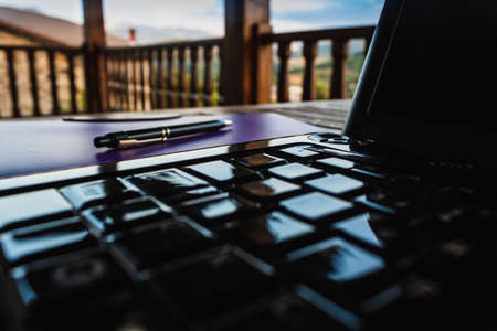 Laptop, notebook and pen on wooden table, landscape background.