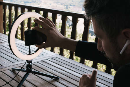 Middle-aged businessman working from home using phone in front of ring light, on the terrace