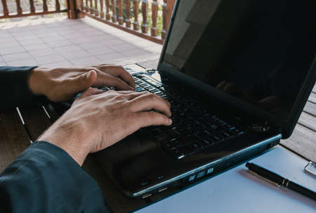 Middle-aged businessman working from home using laptop and notepad on terrace