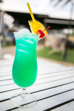 green drink in a tall glass top with coconut decorated by a piece of pineaplle and cherry with straw depth of field backgroundの写真素材