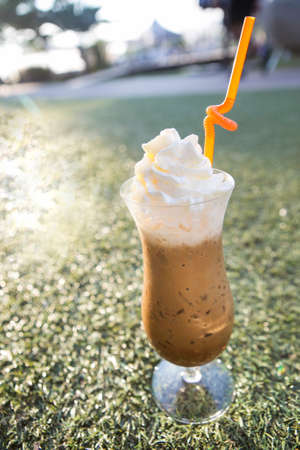iced coffee top with whipped cream in a tall glass on a green grass depth of field backgroundの写真素材
