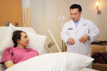 Bangkok, Thailand - September 20,2011 an asian guy doctor is talking to western woman patient who is lay down on bedのeditorial素材