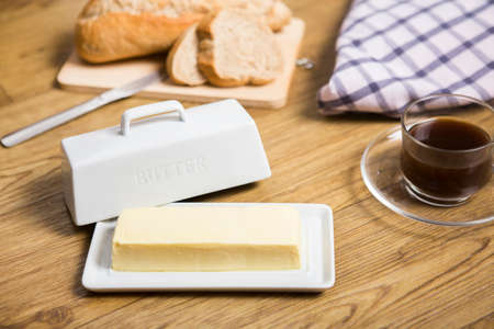 Bangkok, Thailand April 21,2020 natural white modern rectangular ceramic butter dish with holder cover home decor, a cup of coffee, sliced bread and check cloth on the sideのeditorial素材