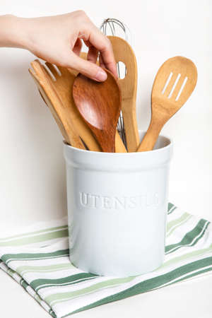 Bangkok, Thailand April 21,2020 hand is taking wood big spoon from a ceramic utensil holder where is putting on striped green table cloth white backgroundのeditorial素材