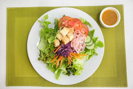 vegetable salad top with ham strips and crouton in white plate served with dressing in a dipping bowl on a green placematの写真素材