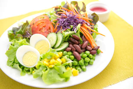 vegetable salad top with boiled egg in white plate served with red dressing in a dipping bowl on a yellow placematの写真素材