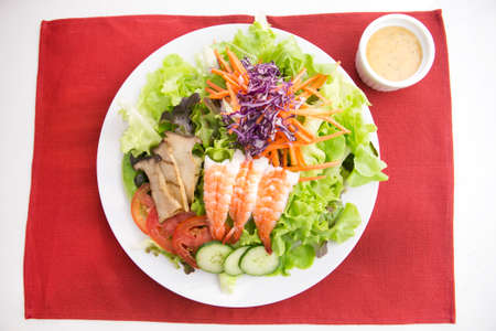 vegetable salad top with shrimps and grilled sliced oringi mushroom in white plate  served with thousand island dressing in a dipping bowl on a red placematの写真素材