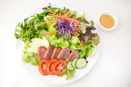 vegetable salad top with sliced roasted duck in white plate  served with thousand island dressing in a dipping bowl on white backgroundの写真素材