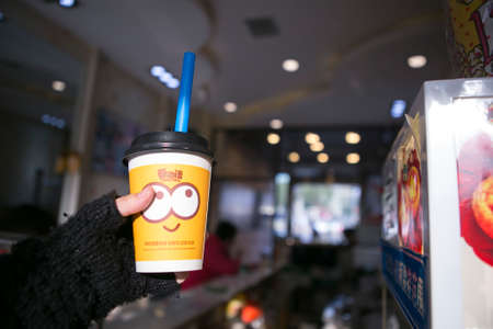 Changsha, China - Feb 20,2014 a takeaway yellow paper cup of tea covered with lid and a blue straw with hand holdingのeditorial素材