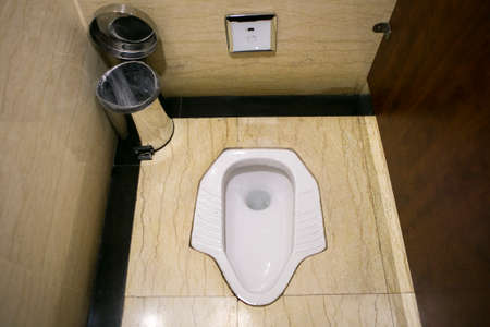 The ancient white squat toilet latrine with stainless steel bin in the corner at Changsha airport, Chinaのeditorial素材