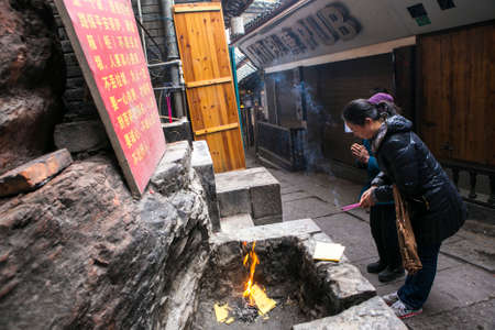 FengHuang, China Feb 21,2014 an asian people are praying one female is holding an incense. They are burning yellow papersのeditorial素材